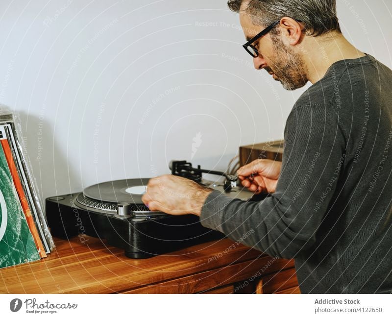 Handsome man listening to music on vinyl record player disc turntable retro vintage nostalgia chill male serious home mature enjoy setting sound song tune