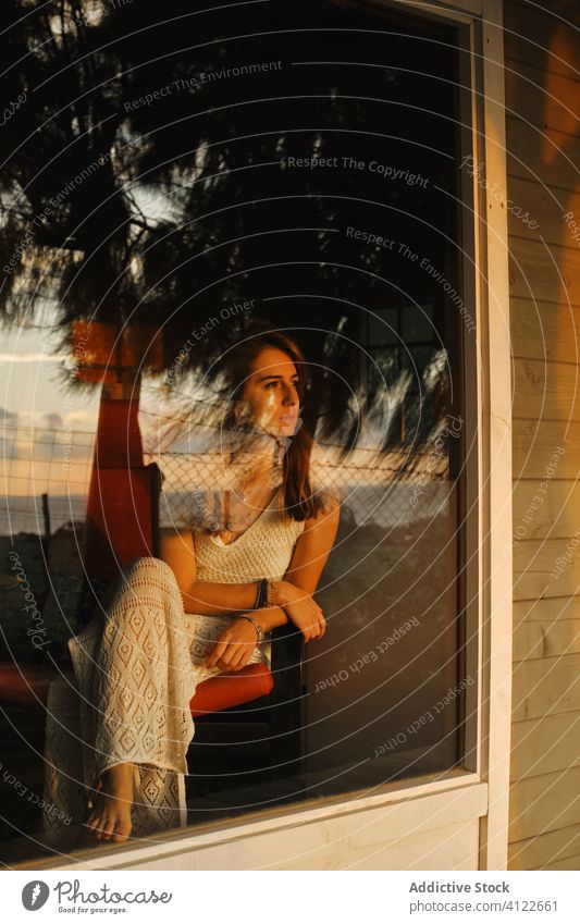 Tranquil woman in armchair relaxing near window admire sunset summer vacation enjoy serene female picturesque house delight cabin wooden sundown chill weekend