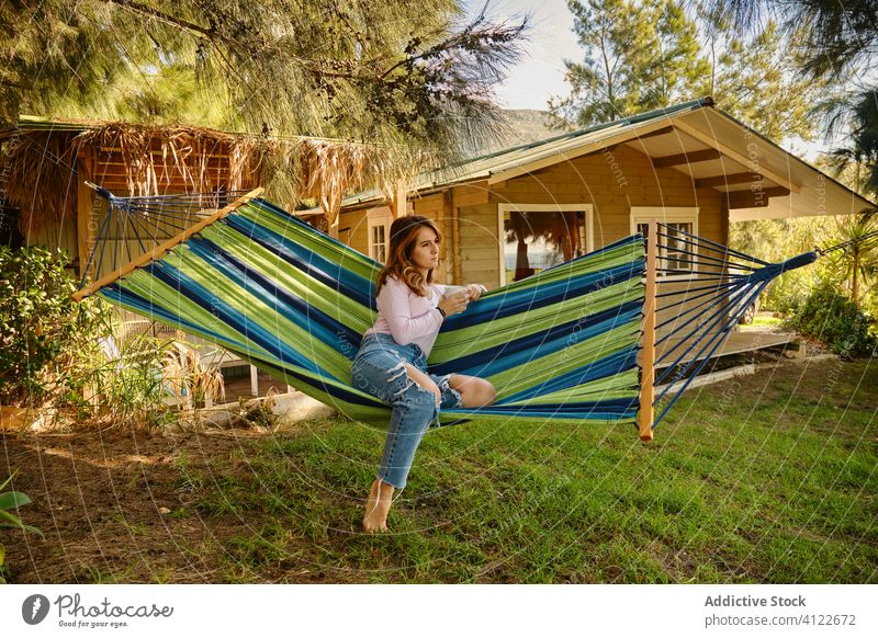 Relaxed woman with cup of coffee in hammock relax hot drink calm lying barefoot courtyard enjoy female summer holiday vacation weekend mug casual outfit