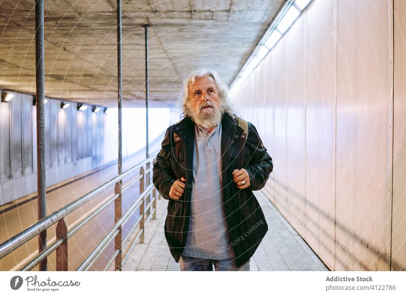 Old aged man walking along sidewalk inside tunnel underground travel senior stroll pedestrian mature carry old tourist urban passage street crosswalk male