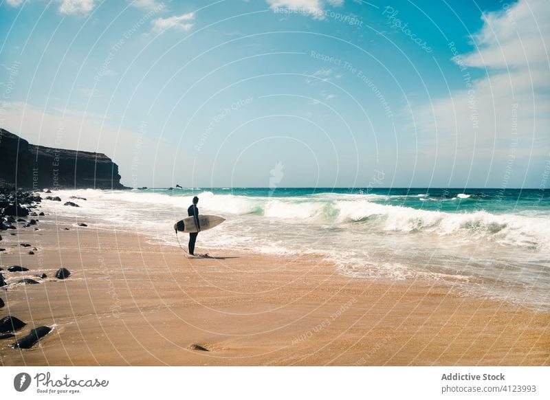 Unrecognizable surfer near waving sea man surfboard beach wave resort hobby fuerteventura spain canary islands sunny daytime water ocean shore coast sand