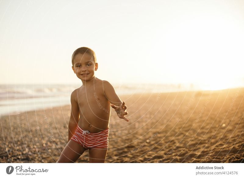 Cheerful boy on beach in evening sea sunset smile resort shirtless summer vacation relax kid lifestyle rest sand cheerful shore joy coast happy glad sundown