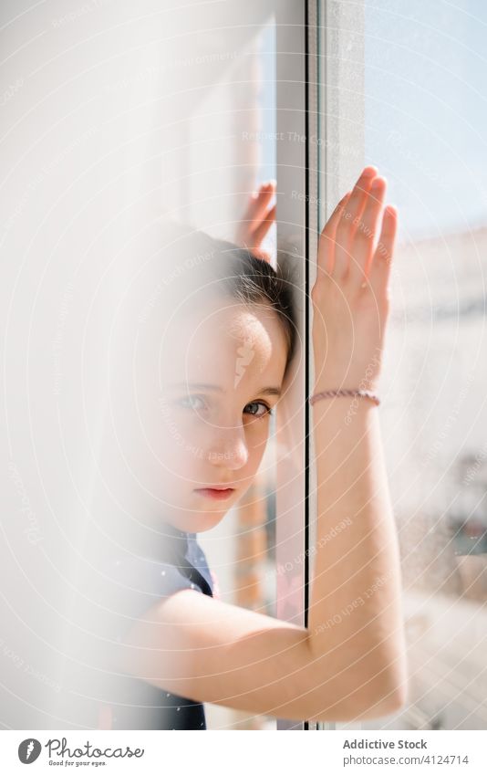 Lonely girl standing near window and looking at camera sad lonely alone quarantine self isolation solitude wait miss dreamy hope social distancing thoughtful