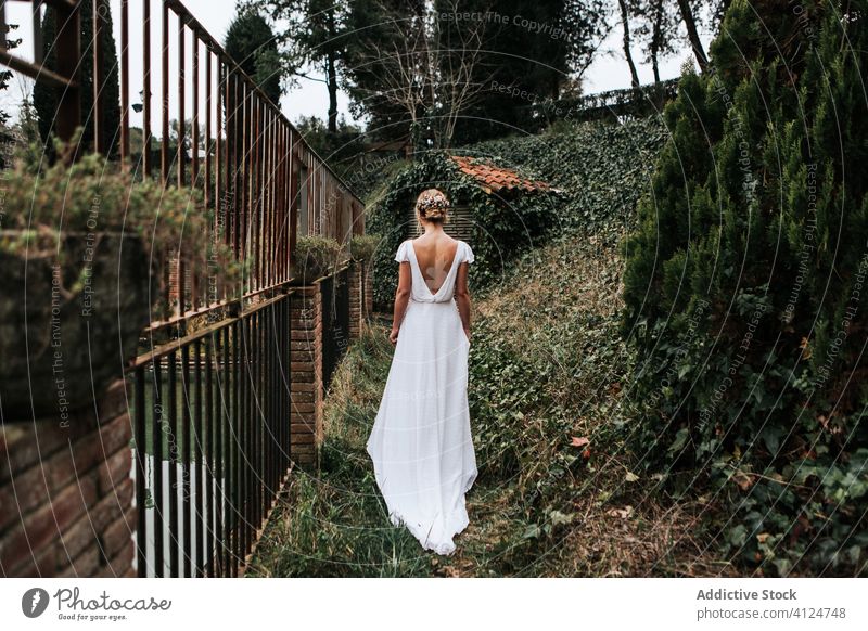 Anonymous bride walking near fence in garden woman wedding elegant summer romantic event female dress white green metal serene celebrate marriage tranquil