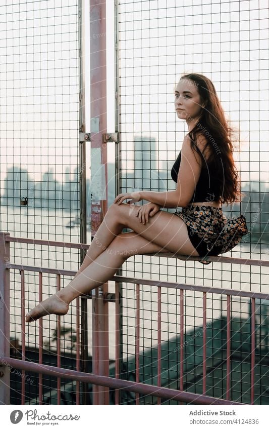 Young female dancer sitting on metal railing of bridge woman grace balance industrial urban cityscape barefoot young tranquil serene calm quiet fence handrail