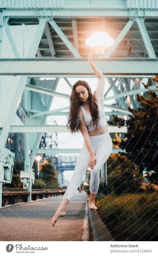 Serene woman in sportswear standing on sidewalk curb in city grace pavement balance serene slim evening female tranquil quiet calm long hair top bra leggings