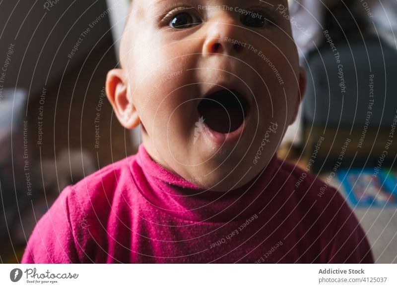 Funny little boy sitting at home and looking at camera amazed wow speechless mouth opened play cheerful cute floor omg charming toddler smile child fun sweet