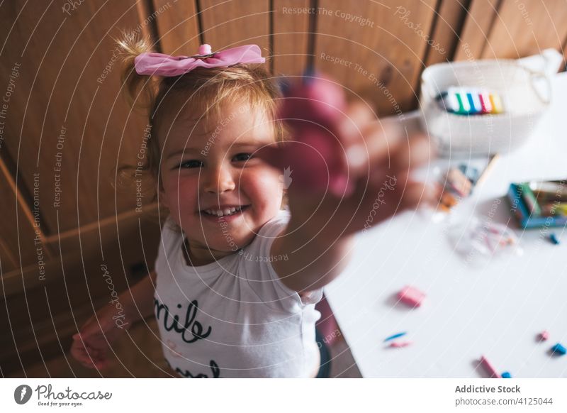 Cheerful cute little girl showing modeling clay at camera toy demonstrate result handmade happy proud charming home play kid smile childhood casual white