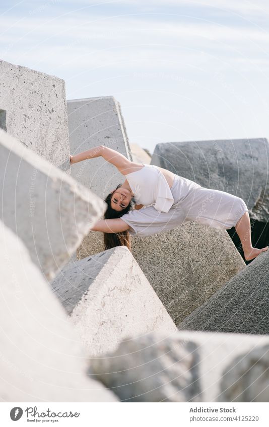 Young woman sitting on stone construction concrete dance sensual power nature harmony contemporary shore coast push modern concept effort young female gray