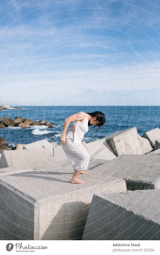 Modern woman standing on concrete block of breakwater sea dance sensual power harmony coast contemporary concept stone construction energy physical young pose