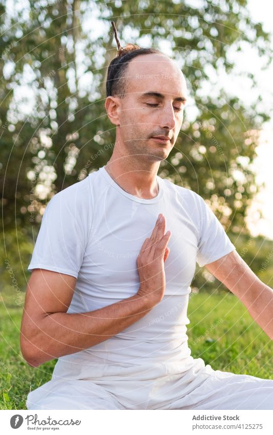 Concentrated young man doing yoga in green field meditate asana calm zen lawn pose summer knee tree park harmony outdoors healthy lifestyle relax peaceful