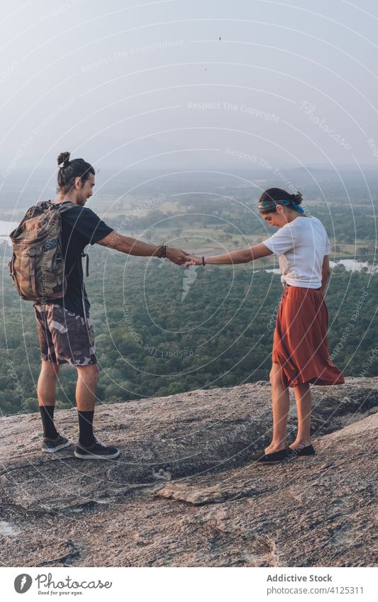 Ethnic couple of backpackers enjoying freedom on hill holding hands hipster sunset travel carefree ethnic sigiriya sri lanka traveler wear stone rocky edge