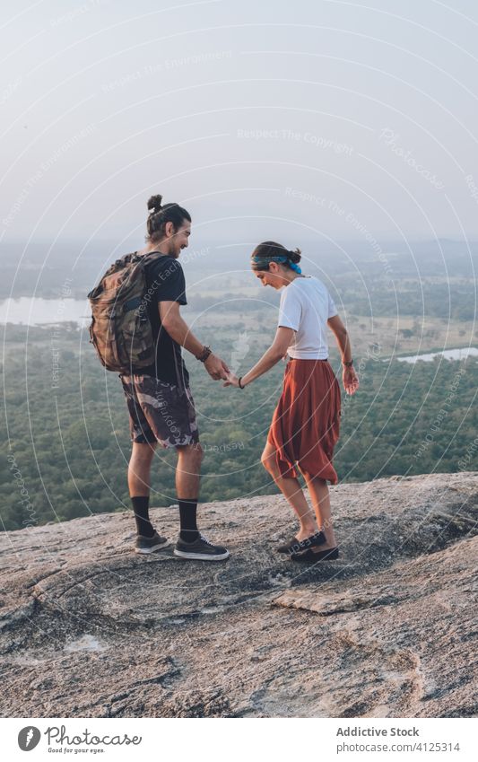 Ethnic couple of backpackers enjoying freedom on hill holding hands hipster sunset travel carefree ethnic sigiriya sri lanka traveler wear stone rocky edge