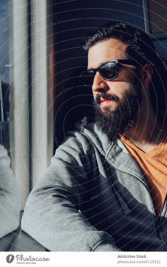 Thoughtful young bearded man looking through window while traveling by train trip dream pensive sunlight summer serious transport passenger seat alone