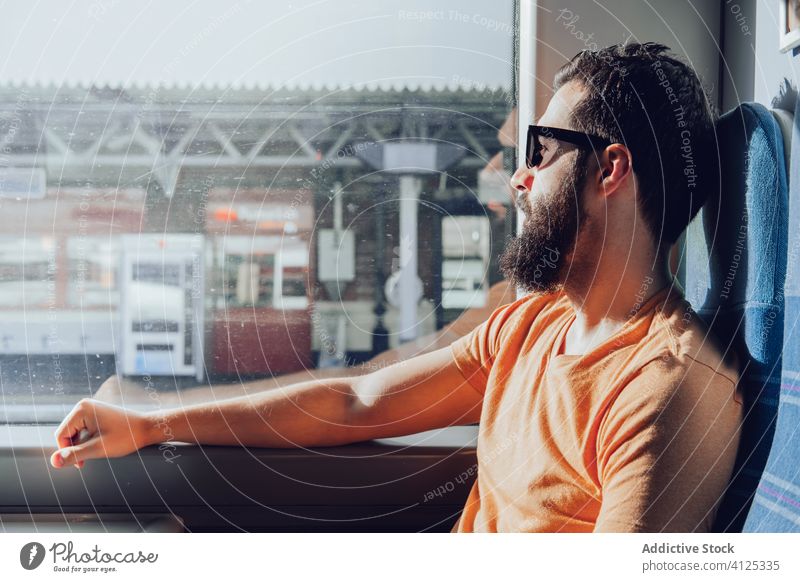 Thoughtful young bearded man looking through window while traveling by train trip dream pensive sunlight summer serious transport passenger seat alone