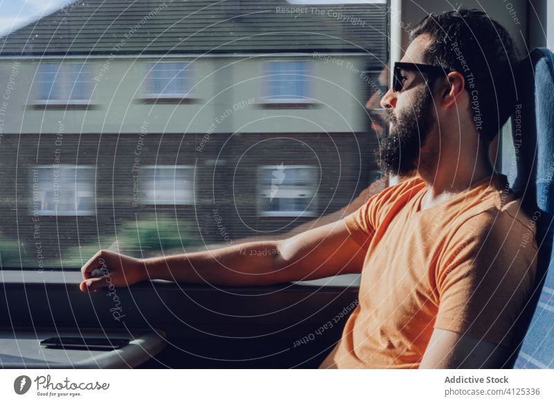 Thoughtful young bearded man looking through window while traveling by train trip dream pensive sunlight summer serious transport passenger seat alone