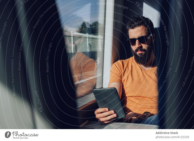 Bearded man in sunglasses browsing smartphone in train tablet passenger commute travel summer mobile transport window beard connection positive young journey