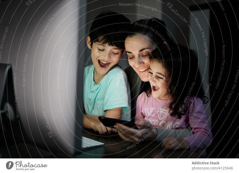 Cheerful woman with kids watching video on computer mother using smartphone together telework childcare happy cheerful home communicate gadget children mom