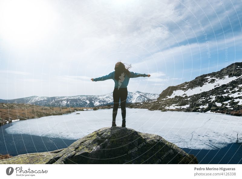 silhouette woman enjoying nature in the top of snowy mountains with a frozen lake in front of her. Winter landscape hiking outdoor adventure sky travel