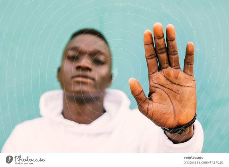 Young african black man against a green wall looking at camera doing a hand stop sign wearing a white sweatshirt with confidence. Selective focus young afro