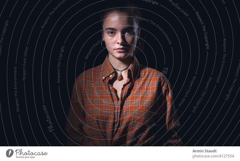 portrait of a beautiful teenage girl with orange plaid shirt woman standing studio serious mysterious human black isolated powerful confident teenager female