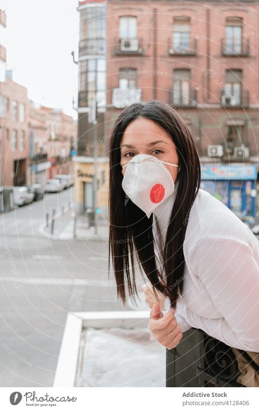 Young woman in respirator mask standing on balcony coronavirus home covid pandemic city self isolation quarantine lockdown female social distancing stay at home