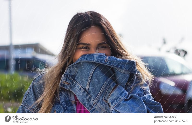 Delighted ethnic female millennial in city street hipster woman delight trendy content denim outfit weekend cover face cheerful glad confident street style