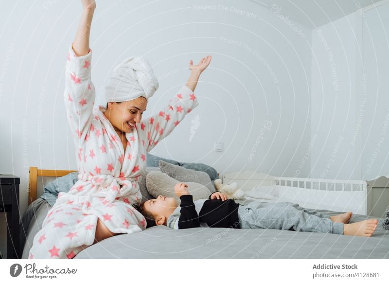 Content mother playing with child in bedroom son having fun together little dressing up game content bathrobe pastime boy parent parenthood mom kid motherhood