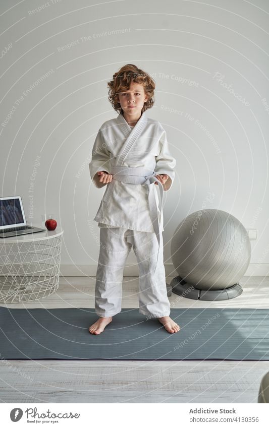 Young boy in white kimono learning judo on laptop at home young online tutorial position practice training childhood activity curly hair computer netbook