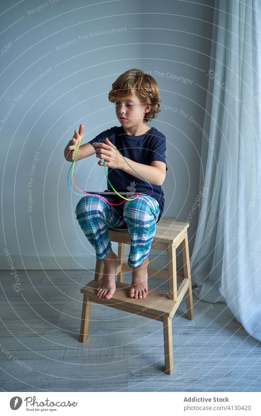 Child with tablet learning cats cradle game kid string play creativity figure stool pajamas home boy focus preteen tie imagination skill develop finger device