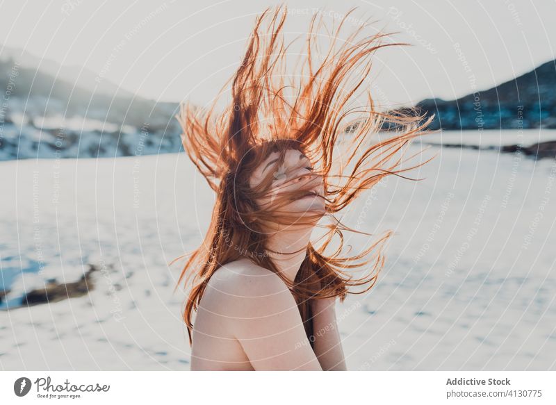 Young woman with hair blowing in wind standing in snowy field red hair topless winter flying hair nature happy relax female bare shoulders valley enjoy naked