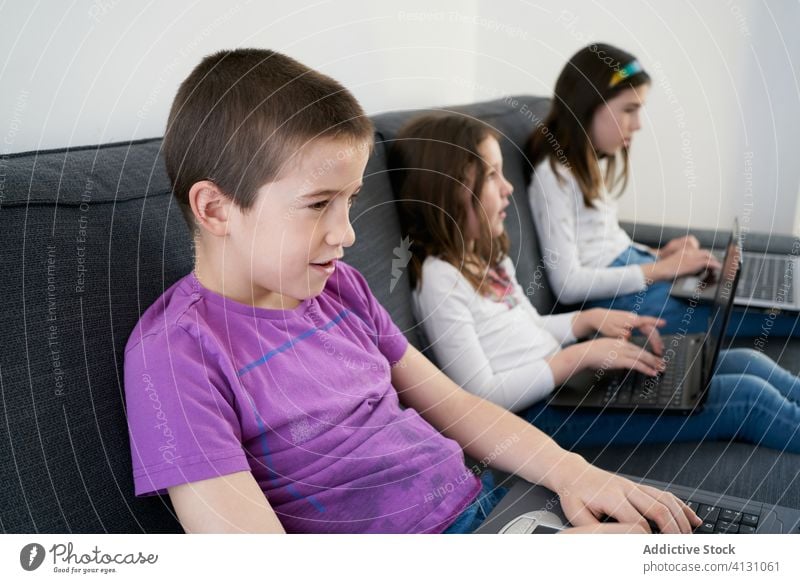 Group of children using laptops while sitting on sofa at home together group room comfort kid internet friendship watch gadget device connection communicate