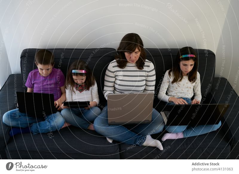 Serious mother and kids spending time together using gadgets on sofa at home children laptop busy addict browsing woman leisure separate sibling parent internet