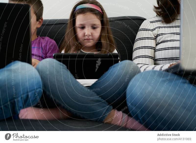 Serious mother and kids spending time together using gadgets on sofa at home children laptop busy addict browsing woman leisure separate sibling parent internet