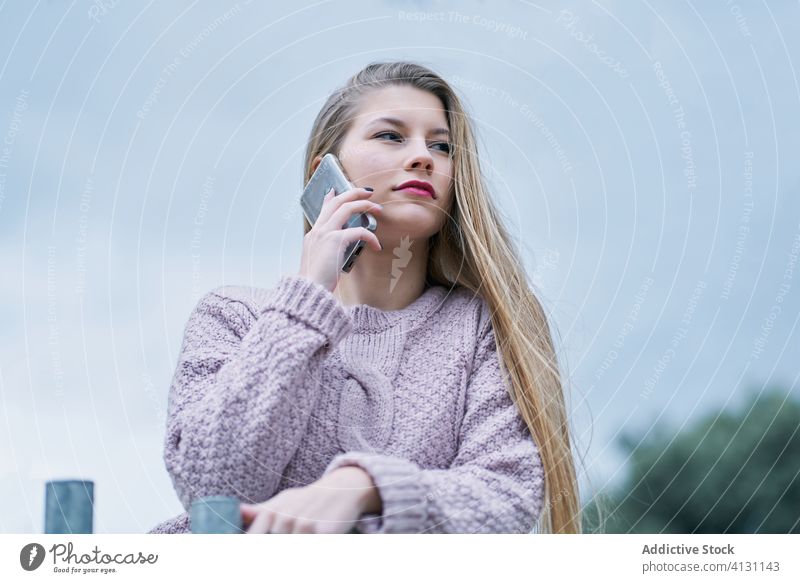 Stylish young lady talking on smartphone against modern building woman thoughtful conversation walk dreamy using city stroll urban device gadget bridge banister