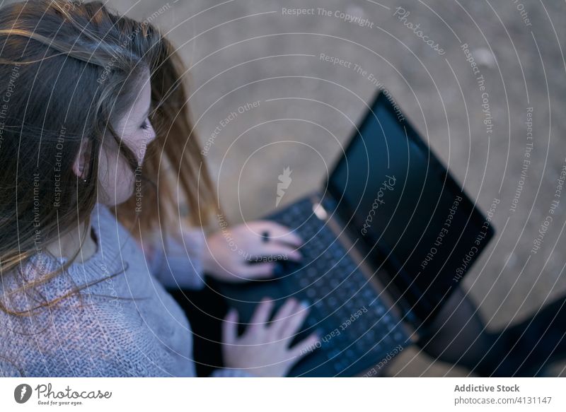 Back view of casual female using laptop on wooden bench in park woman typing email internet device gadget online relax connection rest surfing flowing hair