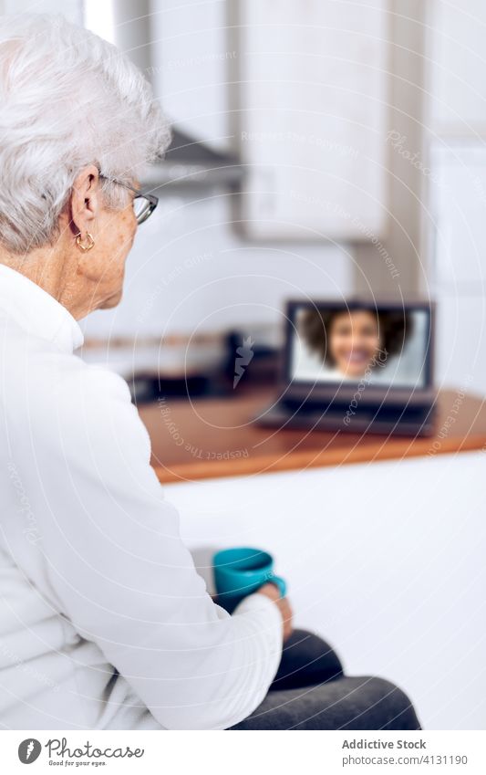 Senior woman drinking tea and talking with daughter on laptop senior video call home coronavirus using online cup kitchen mother mug computer digital