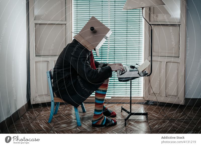 Anonymous male writer typing on old fashioned typewriter cardboard box man retro funny author story vintage antique carton creative eccentric stripe sock style