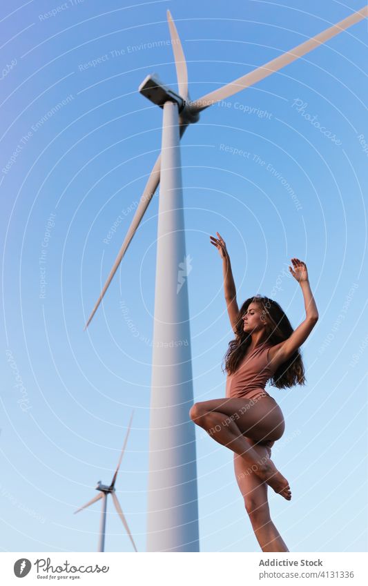 Young slim lady dancing under windmill on sunny day woman bodysuit dance harmony flexible ecology nature environment alone hand up perform balance alternative