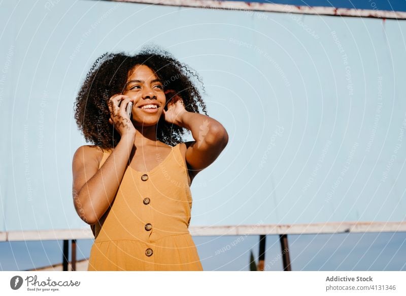 Young satisfied ethnic woman using cellphone on street against empty big board in suburb smartphone billboard use joy banner social media message search watch