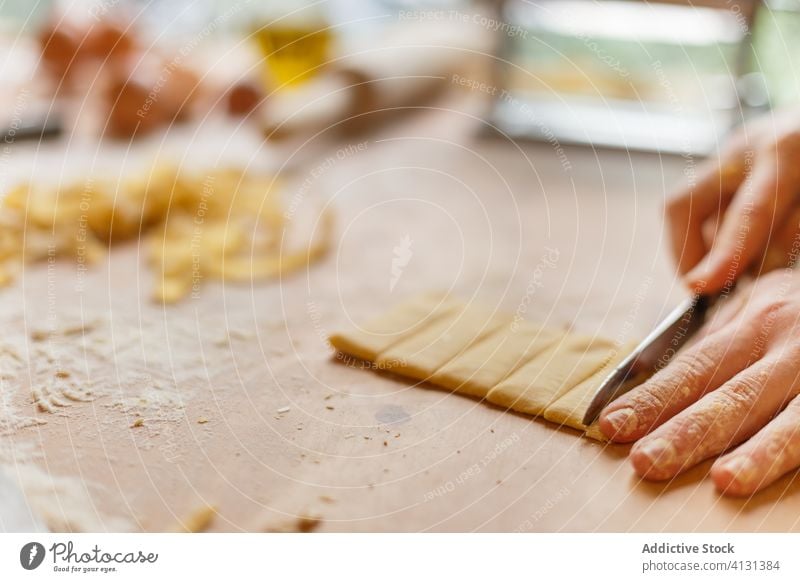 Unrecognizable person cutting pasta dough on table homemade stripe cook thin knife flour prepare kitchen roll process food cuisine culinary recipe handmade chef