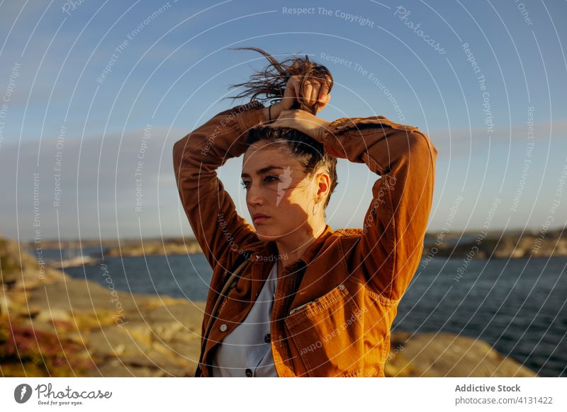 Thoughtful young female tourist standing on rocky seashore and looking away woman traveler harmony dream pensive wave hair wind nature coast vacation thoughtful