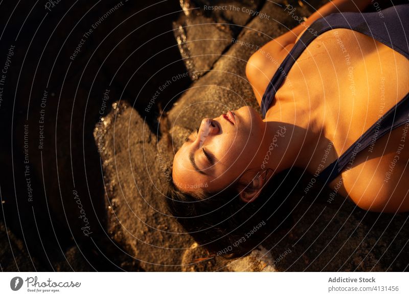 Young woman in swimsuit lying on stone near lake shore sunset relax rocky summer female holiday vacation calm serene tranquil enjoy water harmony peaceful