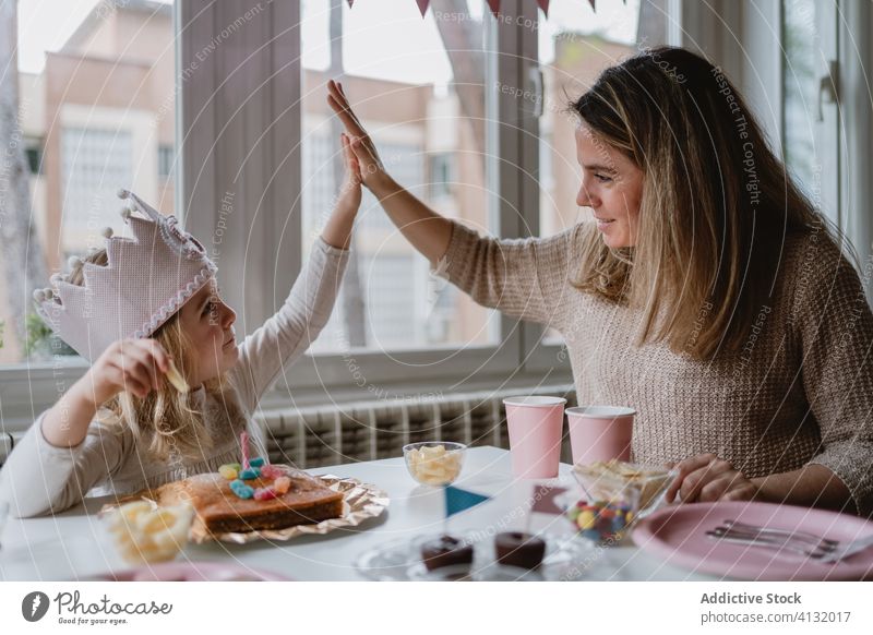 Positive mother giving high five with daughter during party at home girl birthday celebrate fun happy crown princess table holiday kid parent gesture symbol