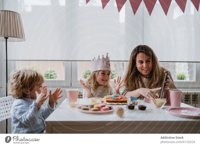 Cheerful little girl making video call on tablet during birthday celebration mother daughter celebrate fun happy remote home distance positive kid mobile phone