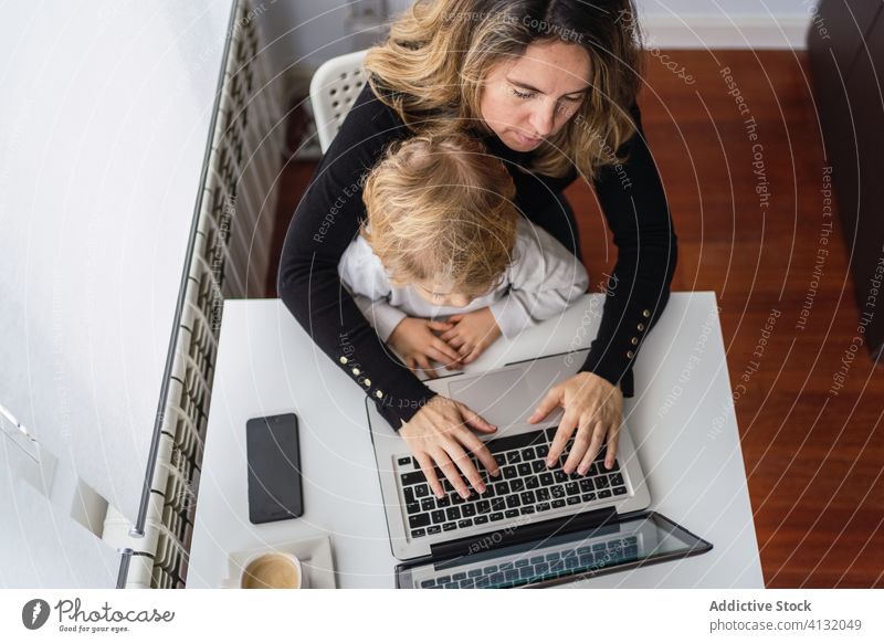 Woman with little kid working on laptop at home woman mother using together online busy remote child curious point motherhood interact parent female