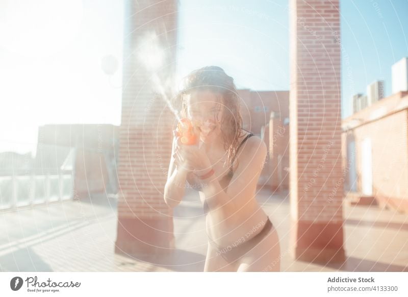 Delighted woman in bikini playing with water gun summer having fun playful pistol wet female swimwear sunny vacation joy holiday relax cheerful smile lady enjoy