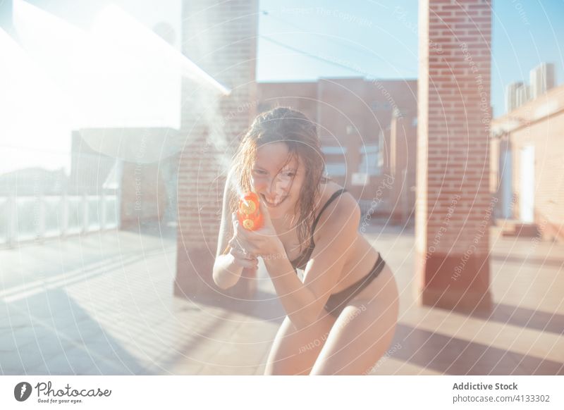 Delighted woman in bikini playing with water gun summer having fun playful pistol wet female swimwear sunny vacation joy holiday relax cheerful smile lady enjoy