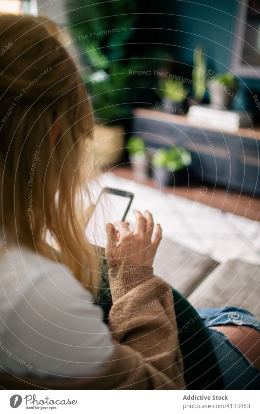 Crop woman browsing smartphone at home surfing cellphone weekend entertain using touch screen female cozy device cushion gadget internet online social media