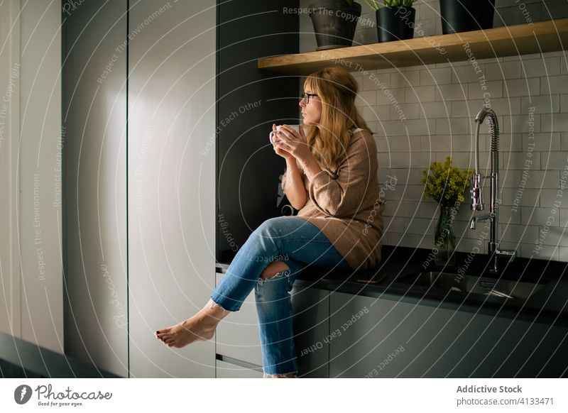 Relaxed woman sitting in kitchen counter drinking coffee thoughtful relax enjoy morning beverage female fresh modern cozy serene pensive home contemporary lady